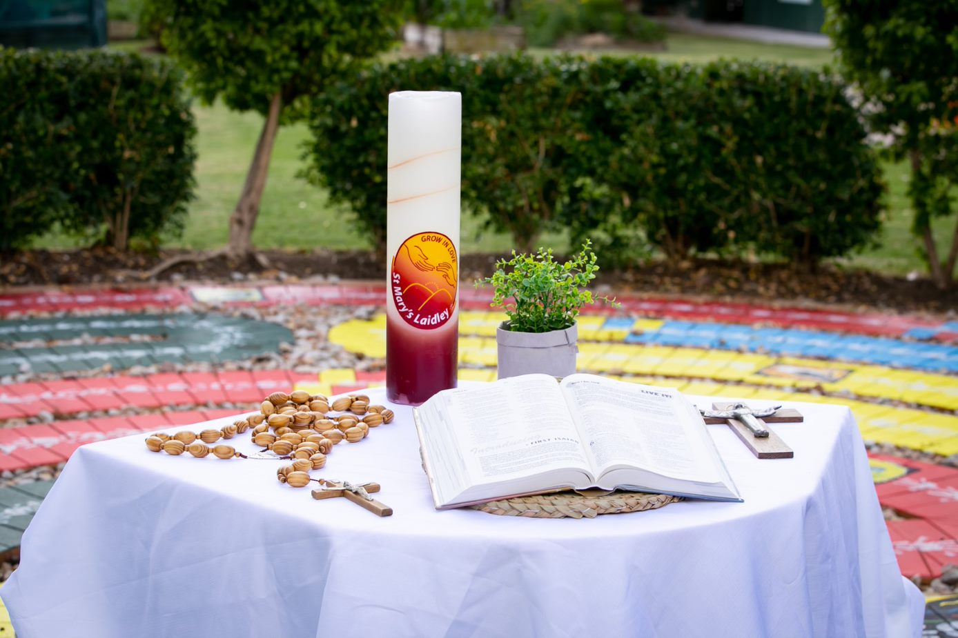 Religious items including a Bible, cross, rosary and candle arranged on a table outdoors.