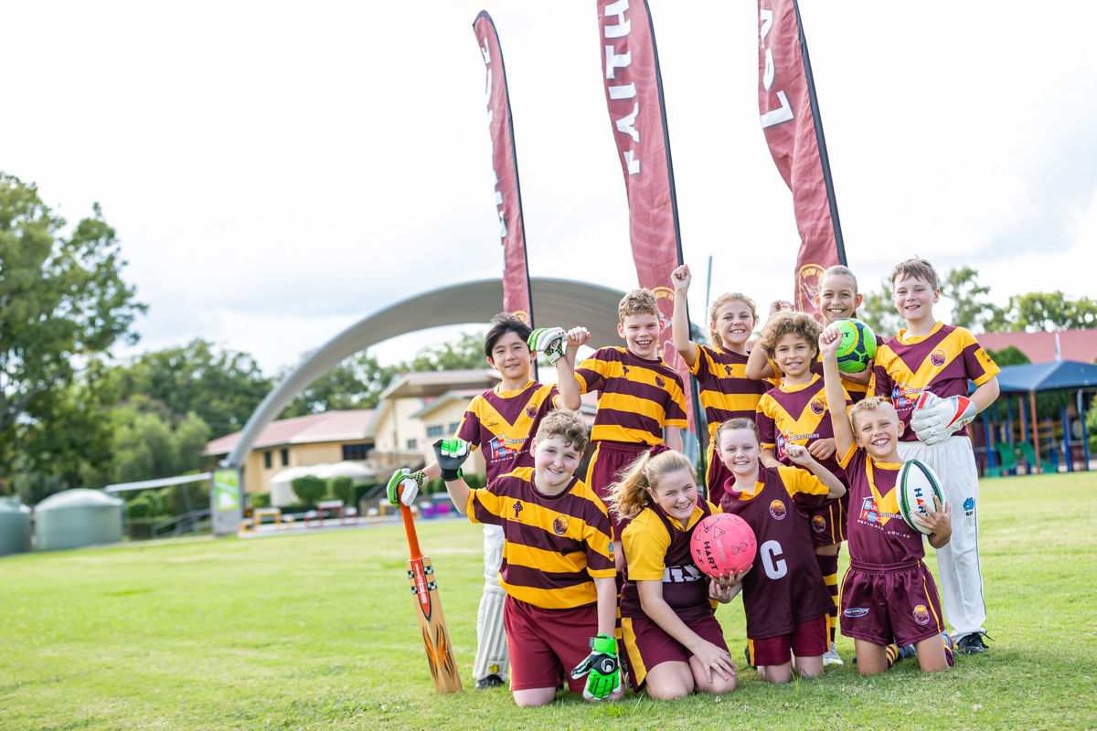 Students in school sports uniforms posing on a field with sporting equipment.